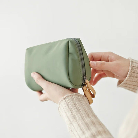 Person holding a green pouch with a beige sleeve on a light background