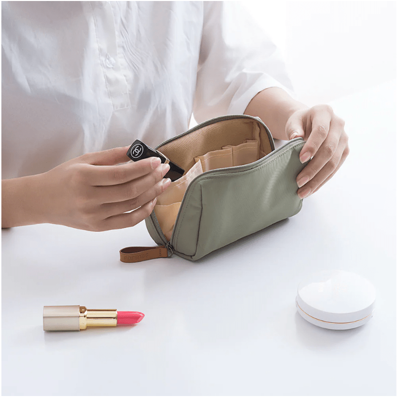 Person organizing a small green travel pouch with cosmetic items on a white surface