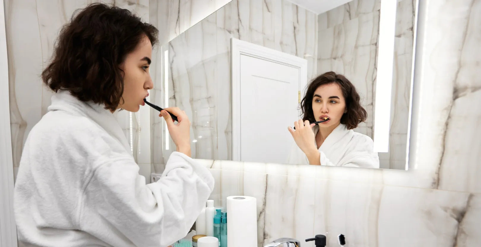 Women brushing her teeth in front of a mirror with OrellaUV Ultra Soft toothbrush